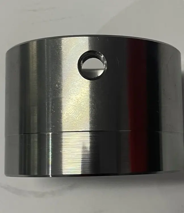 A metal cylindrical bush component with a circular hole in the center, displayed on a white background.